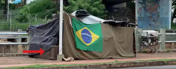 Seta vermelha mostra fio que sai de poste de iluminação para um dos barracos montados na avenida Philadelpho Gouveia Neto, em Rio Preto (Guilherme Baffi 9/4/2024)