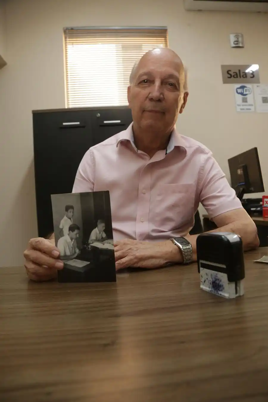 Seu Carlinhos em sua mesa de trabalho com a foto de quando iniciou como cartorário, em setembro de 1958 (Johnny Torres 22/9/2021)